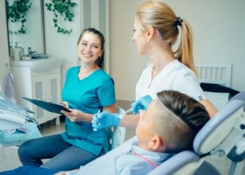 Two dental team members smiling next to young man in dental chair