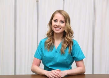 Woman in turquoise scrubs smiling and sitting at desk