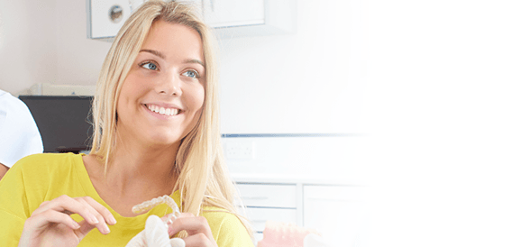 Smiling woman in dental chair holding an Invisalign aligner