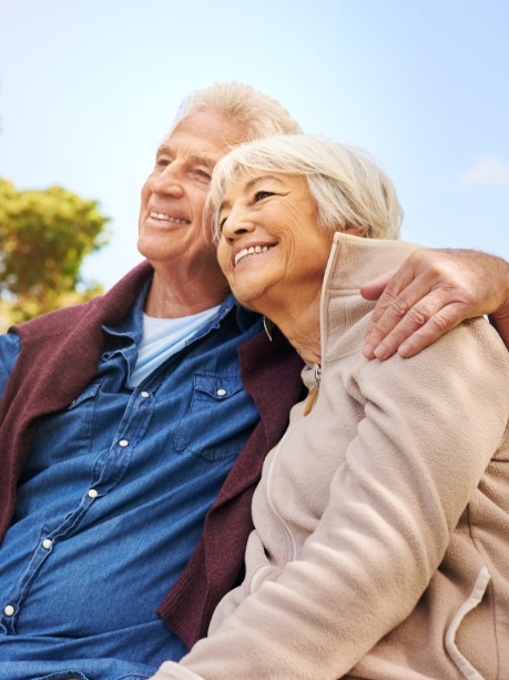 Senior man and woman sitting on park bench and smiling with dentures in Gorham