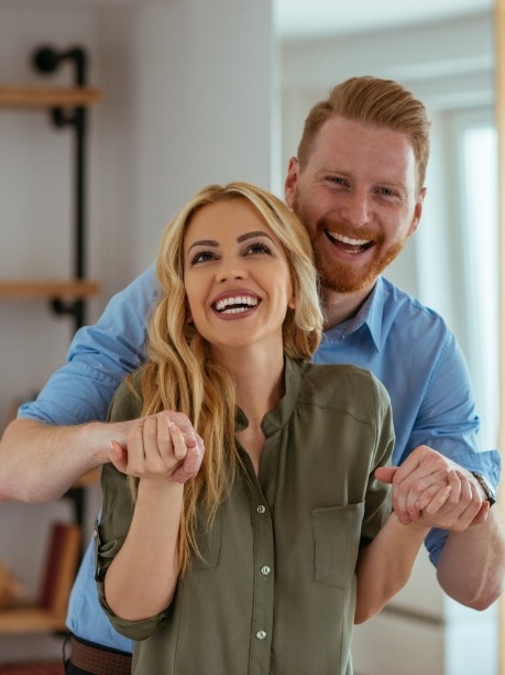 Man and woman in living room holding hands and smiling after dental bonding in Gorham