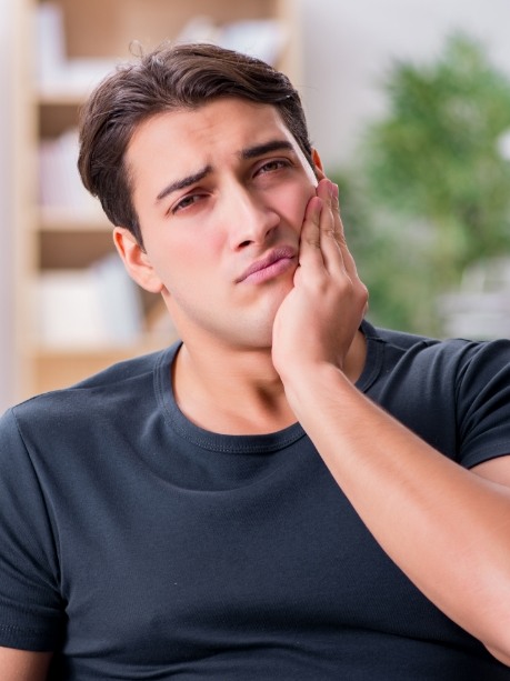 Man wincing and holding his cheek in pain before seeing emergency dentist in Gorham