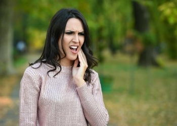 Woman outdoors holding her cheek in pain