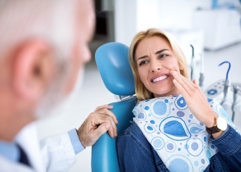 Woman in dental chair holding her cheek in pain