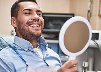 a manking in a handheld mirror at his teeth