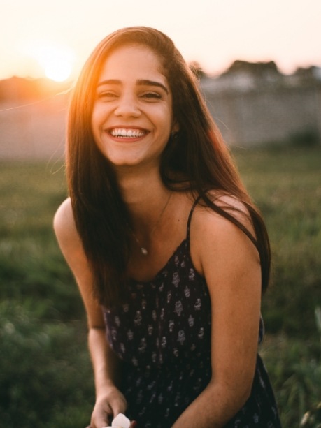 Young woman grinning outdoors after a smile makeover in Gorham