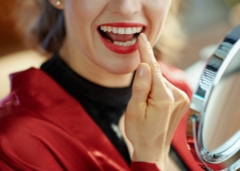 Woman with red lipstick looking at her teeth in mirror