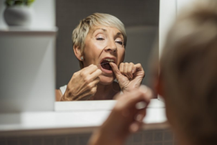 Woman flossing in bathroom mirror