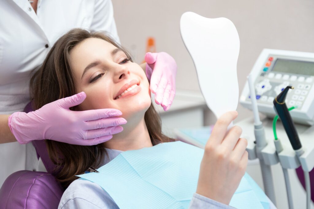 Woman in dental chair smiling at reflection with dentist touching her face