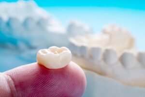 Finger holding a dental crown. 